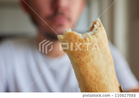 Closeup portrait of hungry man eating delicious sandwich at home on background of kitchen. Handsome male enjoying vegetarian dinner indoors. Caucasian guy eating toast in morning, slow motion. 110827088