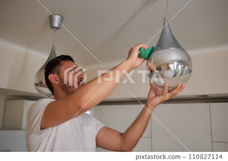 Extreme close-up of unrecognizable man cleaning electric lamp with wet microfiber rag. Close-up of male hands wiping chandelier removing dust at home. Concept of cleaning and household, slow motion. Extreme close-up of unrecognizable man cleaning electric lamp with wet microfiber rag. Close-up of male hands wiping chandelier removing dust at home. Concept of cleaning and household, slow motion. 110827114