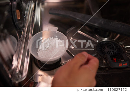 High-angle view of unrecognizable man using funnel to pour granulated salt to soften hard water into dishwasher hole High-angle view of unrecognizable man using funnel to pour granulated salt to soften hard water into dishwasher hole 110827152