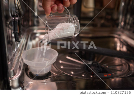 High-angle view of unrecognizable man using funnel to pour granulated salt to soften hard water into dishwasher hole High-angle view of unrecognizable man using funnel to pour granulated salt to soften hard water into dishwasher hole 110827156