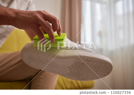 Cleaning suede sneakers. A worker in a shoe workshop cleans a pile of shoes Cleaning suede sneakers. A worker in a shoe workshop cleans a pile of shoes 110827356