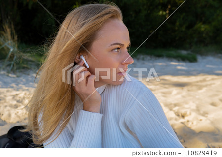 Happy young woman on the beach sea ocean. Wearing wireless headphones doing audio healing sound therapy being mindful Leisure in nature. Wellbeing unity with nature health mindfulness Happy young woman on the beach sea ocean. Wearing wireless headphones doing audio healing sound therapy being mindful Leisure in nature. Wellbeing unity with nature health mindfulness 110829419