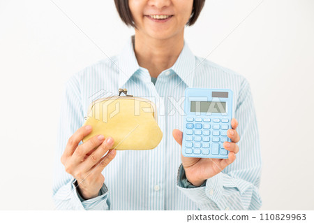 A middle-aged woman smiling while holding a blue calculator and purse A middle-aged woman smiling while holding a blue calculator and purse 110829963