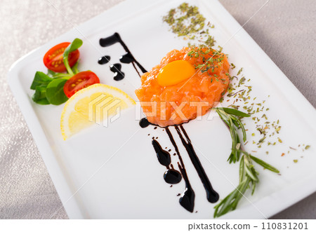 Fresh tartar with salmon, balsamic, greens and lemon on white plate 110831201