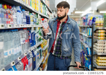 Portrait of focused young man purchasing bottled water in grocery store 110831276