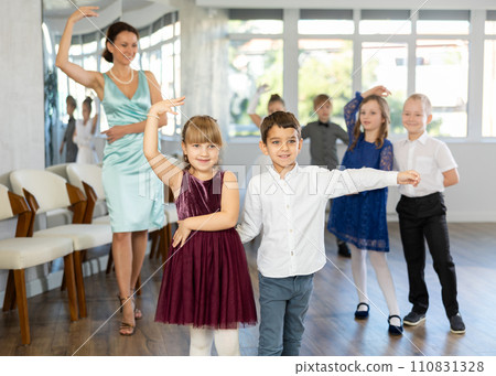Little children in elegant dresses practicing waltz dance in school hall 110831328