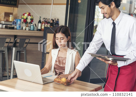 Restaurant business Handsome waiter serving food to young beautiful women with smiling face. Businesswoman using computer laptop while working on luch time. Waiter Man serving coffee cup in cafe Restaurant business Handsome waiter serving food to young beautiful women with smiling face. Businesswoman using computer laptop while working on luch time. Waiter Man serving coffee cup in cafe 110832141