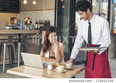 Restaurant business Handsome waiter serving food to young beautiful women with smiling face. Businesswoman using computer laptop while working on luch time. Waiter Man serving coffee cup in cafe Restaurant business Handsome waiter serving food to young beautiful women with smiling face. Businesswoman using computer laptop while working on luch time. Waiter Man serving coffee cup in cafe 110832148