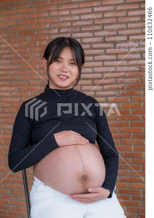 Mom pregnant woman in a dress holds hands on belly on red brick background, Waiting for the birth of your baby with love 110832466