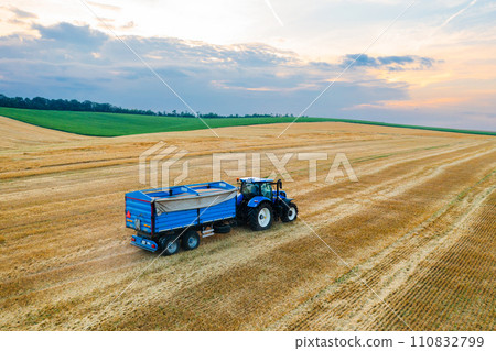 A tractor hauling a trailer cruises across a harvested agricultural field from an aerial perspective 110832799