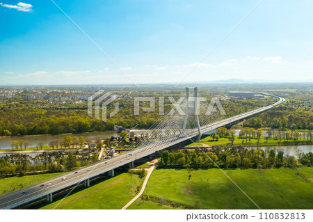 Cars drive on cable-stayed bridge under clear blue sky. Massive Redzinski Bridge over Oder river in sunny spring leading to Wroclaw aerial view Cars drive on cable-stayed bridge under clear blue sky. Massive Redzinski Bridge over Oder river in sunny spring leading to Wroclaw aerial view 110832813