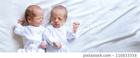 Newborn twins on the bed,on a white background. Life style, emotions of kids. Banner Newborn twins on the bed,on a white background. Life style, emotions of kids. Banner 110833358