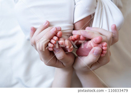 Mom and dad hands hold small legs of their two newborn twin babies 110833479