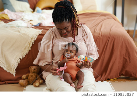 Black woman sitting on floor and playing with baby girl sucking pacifier Black woman sitting on floor and playing with baby girl sucking pacifier 110833827