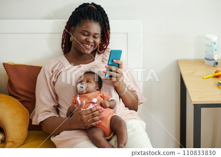 Cheerful Black woman with newborn baby texting friends Cheerful Black woman with newborn baby texting friends 110833830