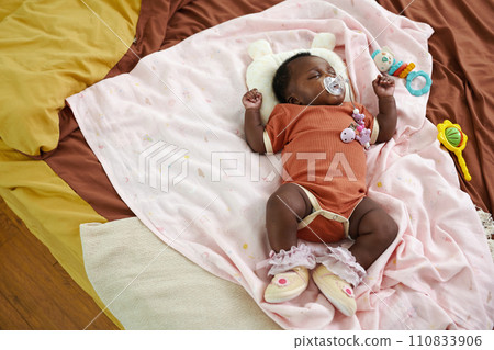 Black newborn baby sleeping on bed and sucking pacifier, top view 110833906