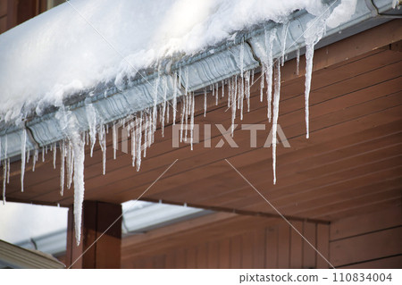 Collection of icicles hanging from the edge of a roof Collection of icicles hanging from the edge of a roof 110834004