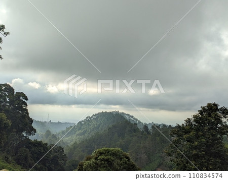 The road is in the middle of forests and mountains which are cloudy and cool 110834574