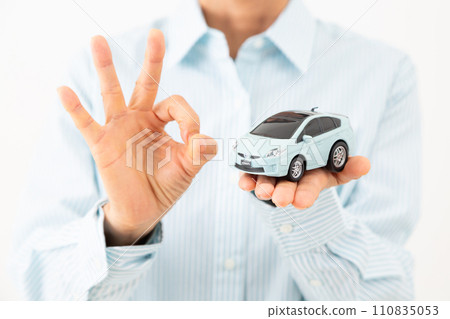 A middle-aged woman holding a car model and making a circle sign 110835053