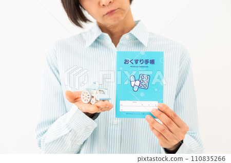 A middle-aged woman worries while holding a medicine notebook and a model of a wheelchair. A middle-aged woman worries while holding a medicine notebook and a model of a wheelchair. 110835266