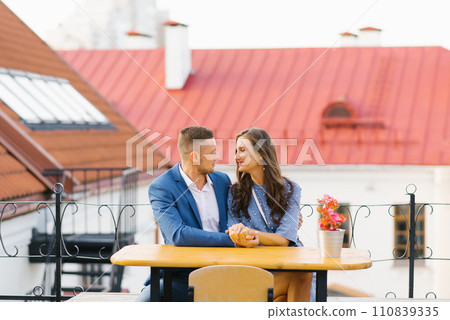 Beautiful couple in love is sitting at a table in an outdoor cafe on a date Beautiful couple in love is sitting at a table in an outdoor cafe on a date 110839335