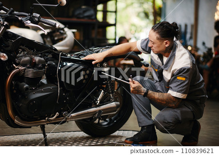 Repairman fixing motorcycle in modern garage Repairman fixing motorcycle in modern garage 110839621