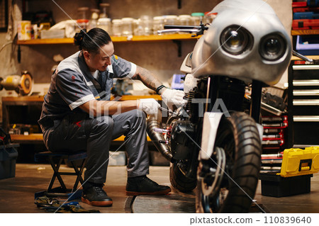 Mechanic in uniform repairing motorcycle of client Mechanic in uniform repairing motorcycle of client 110839640