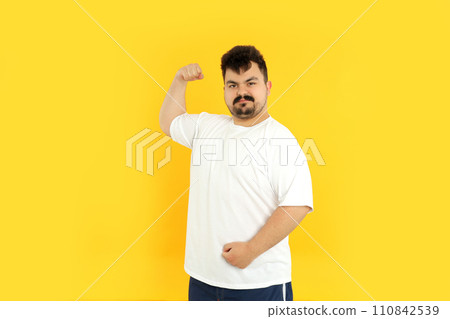 A fat man shows his muscles, on a yellow background. A fat man shows his muscles, on a yellow background. 110842539