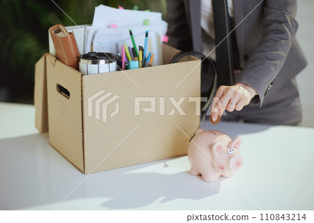 Woman employee in green office putting coin into piggy bank Woman employee in green office putting coin into piggy bank 110843214