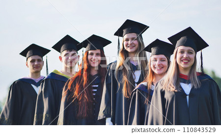 Cheerful graduates pose with raised diplomas on a sunny day. Cheerful graduates pose with raised diplomas on a sunny day. 110843529