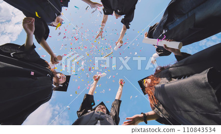 Happy graduates throwing up colorful confetti against the blue summer sky. Happy graduates throwing up colorful confetti against the blue summer sky. 110843534
