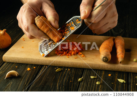 A grater in the chef's hand for grating carrots. Concept of preparing vegetable dish on kitchen table for lunch 110844908