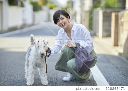 一名年輕女子帶著一隻剛毛獵狐犬在住宅區散步 一名年輕女子帶著一隻剛毛獵狐犬在住宅區散步 110847471
