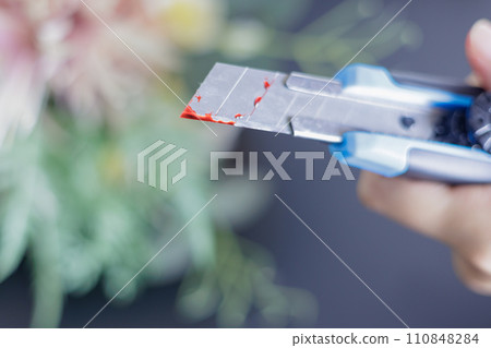 Woman's hand holding a bloody cutter and a bouquet of flowers Woman's hand holding a bloody cutter and a bouquet of flowers 110848284