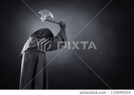 Man in black hooded cloak with axe over dark misty background 110848503