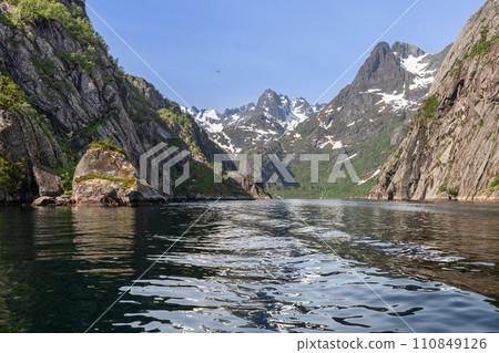 Trollfjorden's steep cliffs and mountains, with snow veins, under a blue sky and a flying bird Trollfjorden's steep cliffs and mountains, with snow veins, under a blue sky and a flying bird 110849126