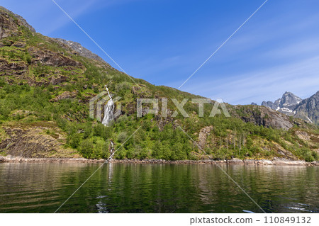 Crystal waters fall into a calm fjord, set against Trollfjorden's lush summer greenery 110849132