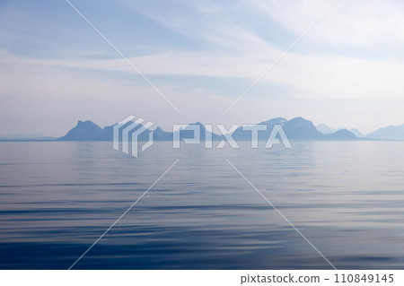 A serene view of the Lofoten Islands' silhouette under a pastel azure sky, reflected gently sea 110849145