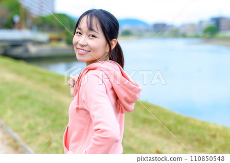 Young woman jogging outside along the river, diet running wear, trimmed up 110850548