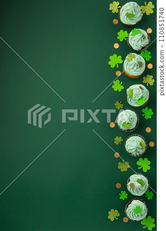 St. Patrick's Day vanilla and chocolate cupcakes with green frosting and  shiny clover decorations on green paper background. Irish holiday dessert concept. Top view, copy space. 110851740