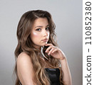 A beautiful brown-eyed girl in an evening dress, with makeup and long hair. 110852380