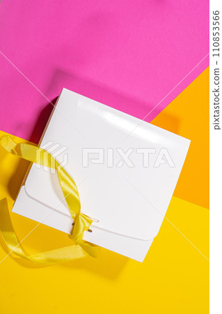 Simple white cardboard box with yellow ribbon on color background, top view 110853566