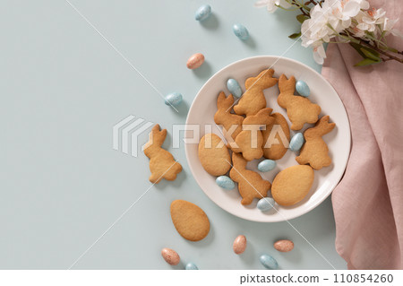 Homemade Easter bunnies shaped cookies and chocolate eggs on blue background. Top view. Space for text. Festive food and snacks. Greeting card. 110854260