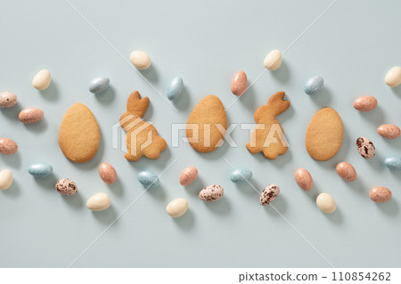 Easter glazed cookies shaped of bunny and chocolate sweets candy as eggs on blue background. View from above. Festive food and snacks. Greeting card. 110854262
