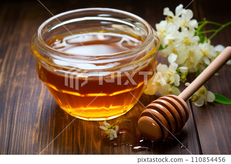 Golden acacia honey in glass bowl with honey dipper and flowers. 110854456
