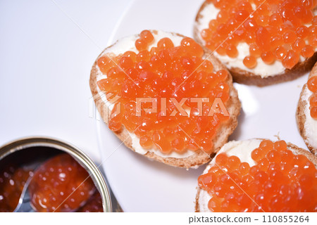 Red salmon caviar on bread and butter. A spoon with red caviar. Red salmon caviar on bread and butter. A spoon with red caviar. 110855264