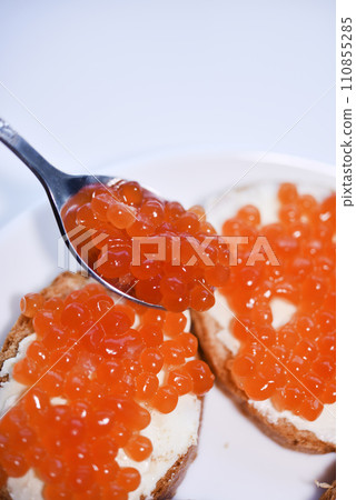 Red salmon caviar on bread and butter. A spoon with red caviar. Red salmon caviar on bread and butter. A spoon with red caviar. 110855285