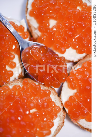 Red salmon caviar on bread and butter. A spoon with red caviar. Red salmon caviar on bread and butter. A spoon with red caviar. 110855286