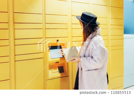 Fashion woman with box using modern postal automatic mail terminal with self service device for pickup or refund an order. Electronic locker for storing parcels. Online shopping. Selective focus. 110855513