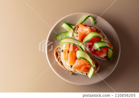 Sandwiches with smoked trout, cream cheese, fresh cucumber and capers on a beige background. 110856205
